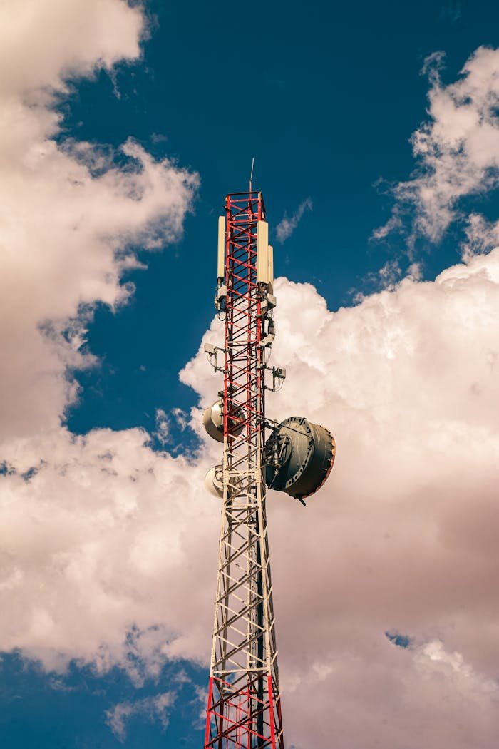 Tall telecommunication tower reaching into blue cloudy sky, symbolizing connectivity and communication.